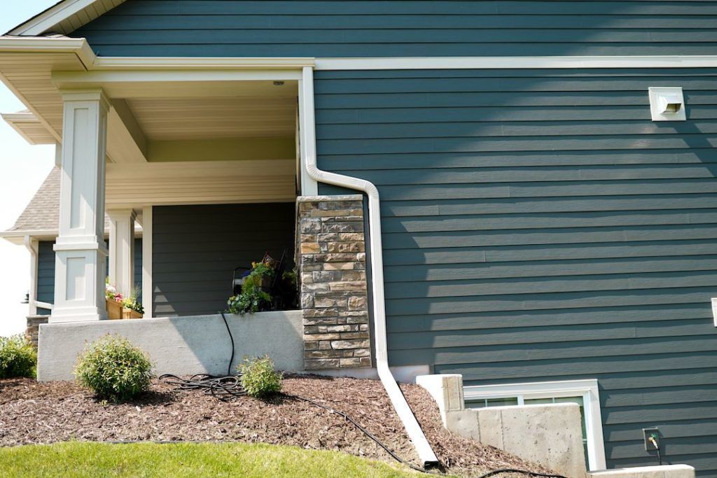 Suburban house exterior with dark blue siding, stone columns, and a small landscaped front slope