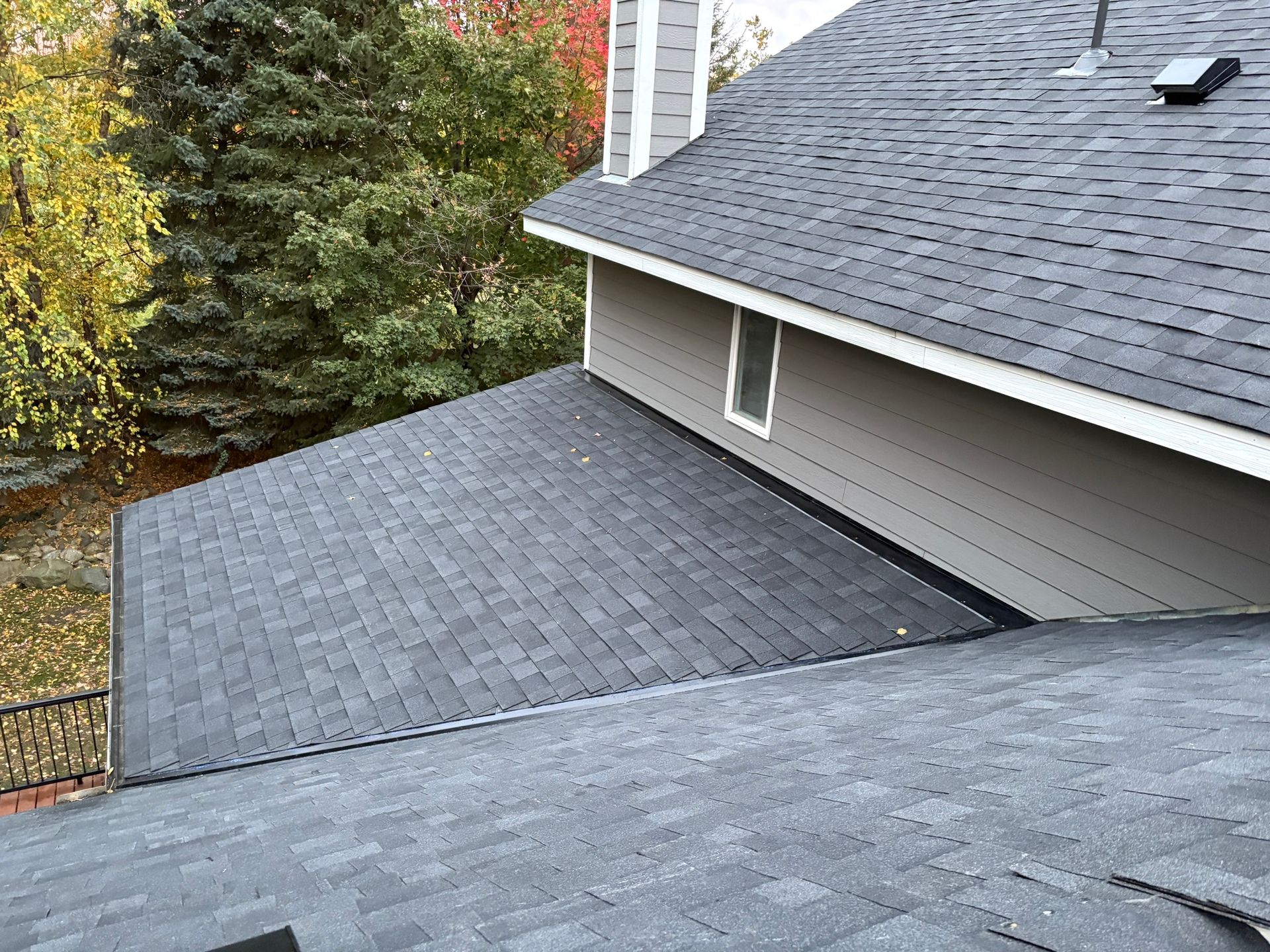 Gray shingled roof sections on a house, viewed from above with trees in the background