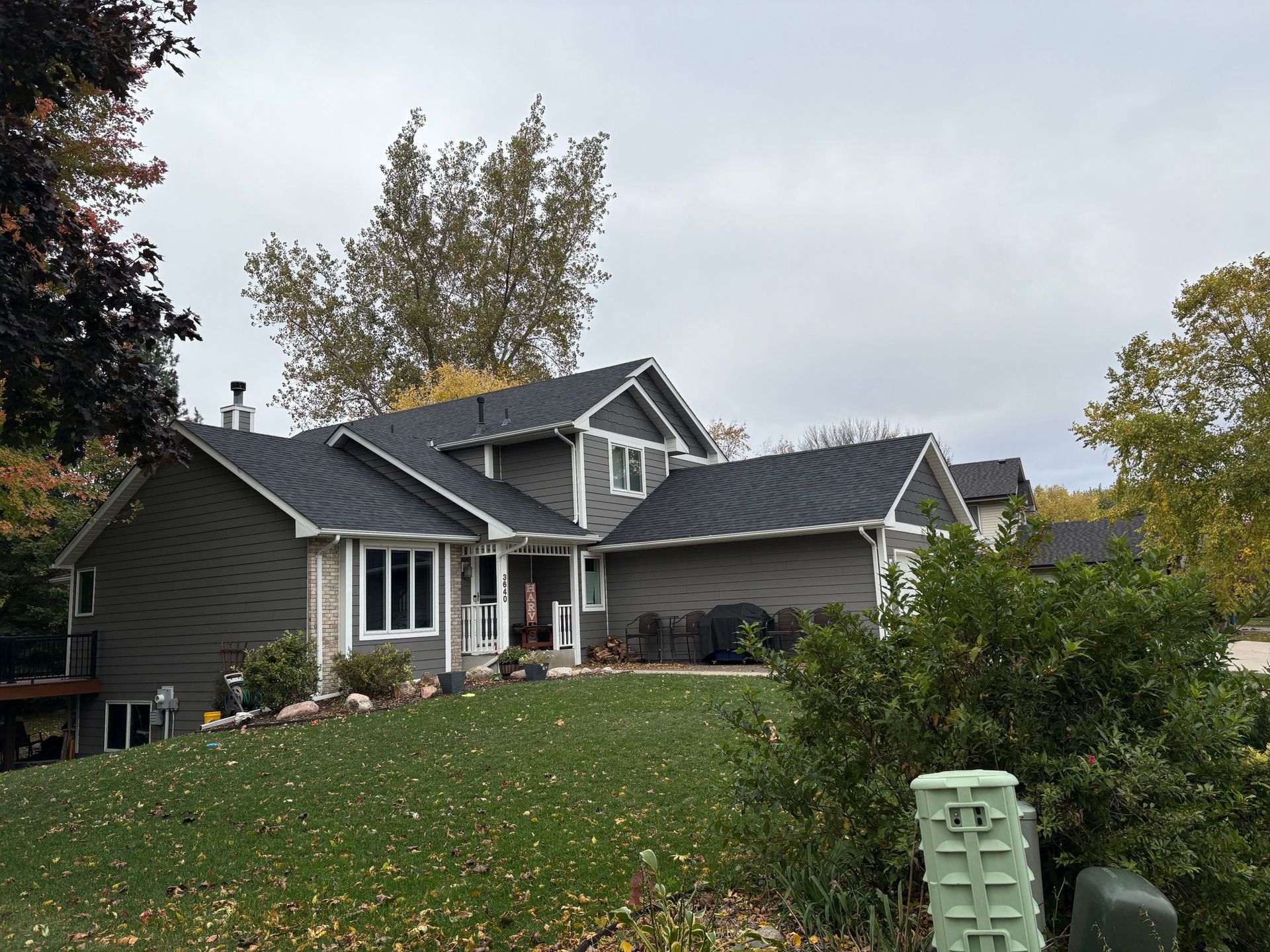 Suburban house with dark roof and stone facade on a grassy slope under cloudy sky