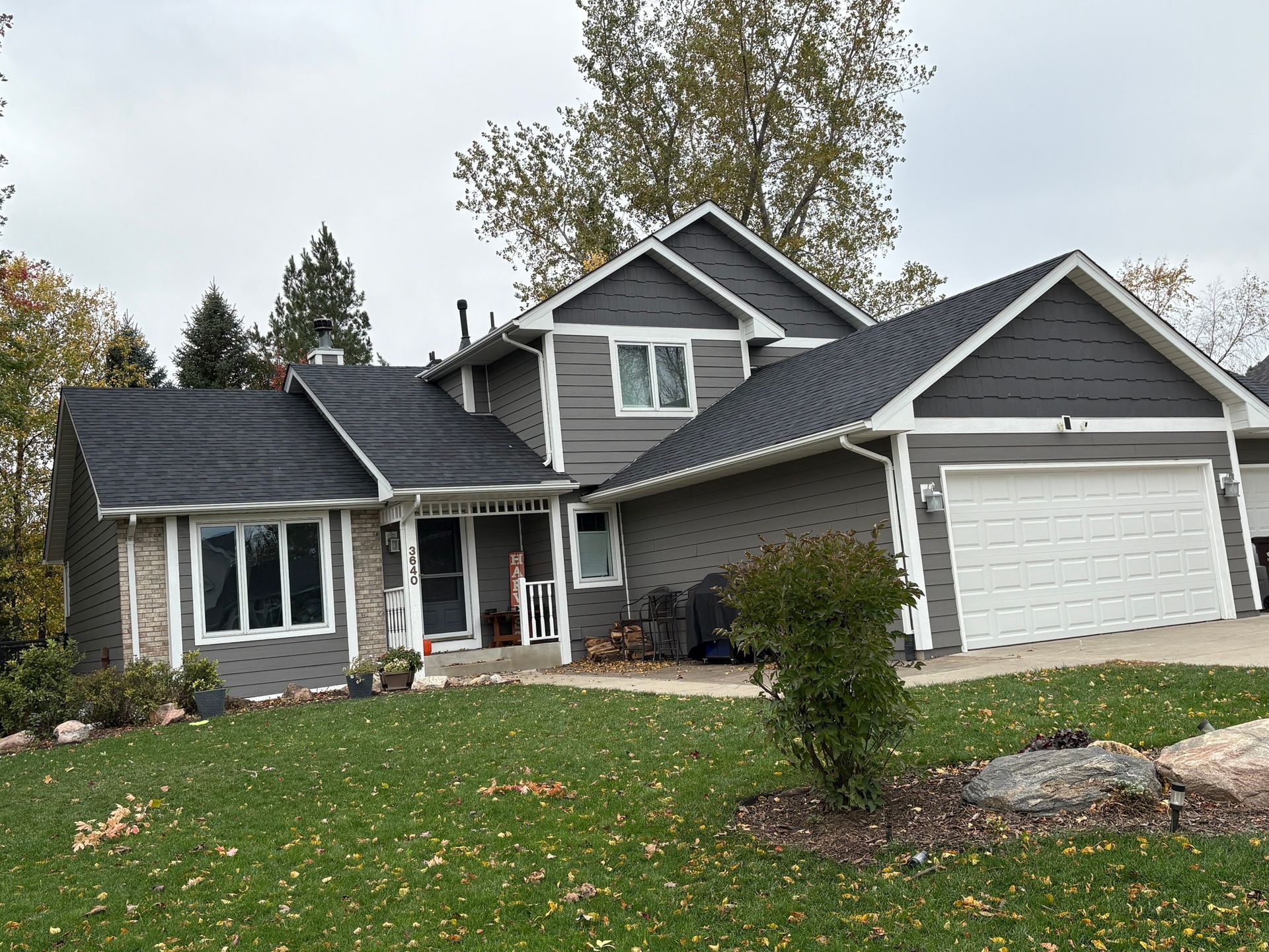 Suburban house with gray siding, white garage, and front lawn in autumn
