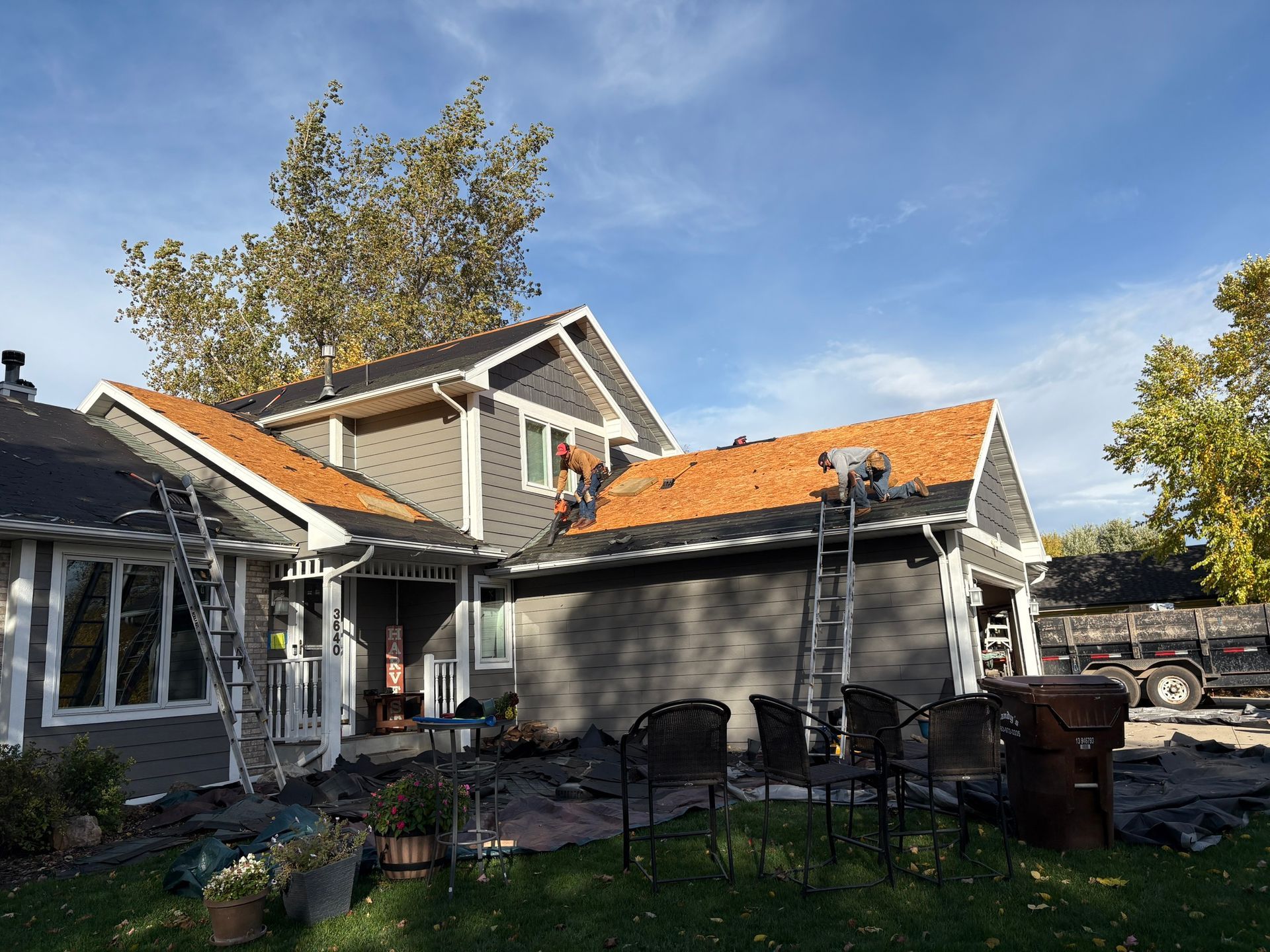 Backyard patio beside a house with orange roof tiles and outdoor furniture under a blue sky