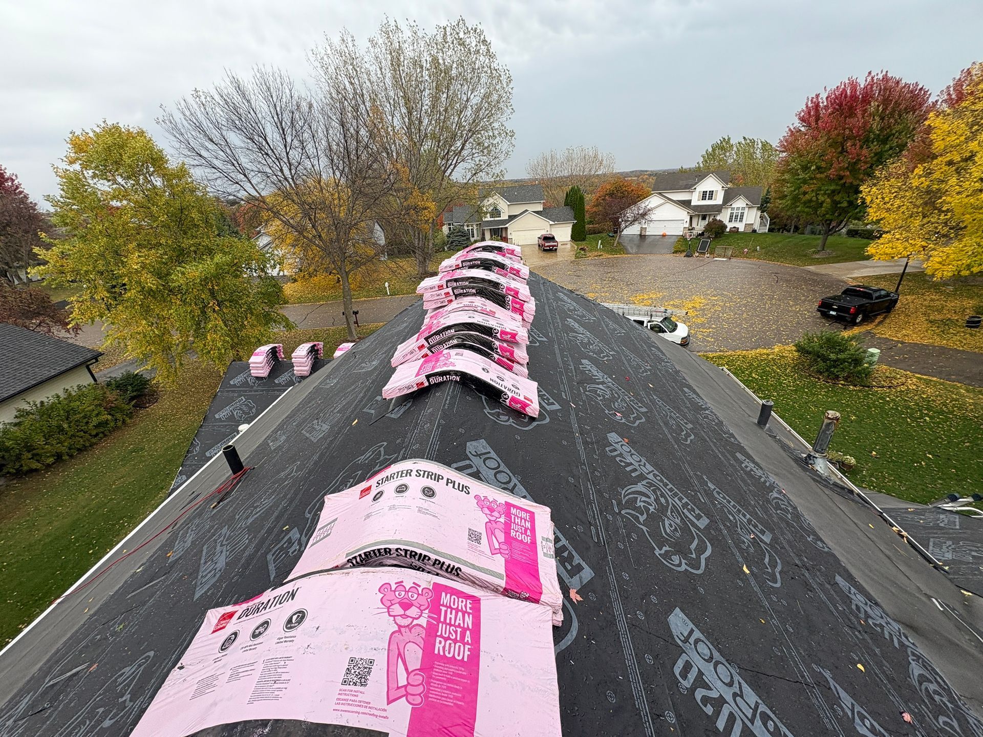 Roof under repair with pink insulation sheets and workers on a sloped black roof, autumn trees nearby