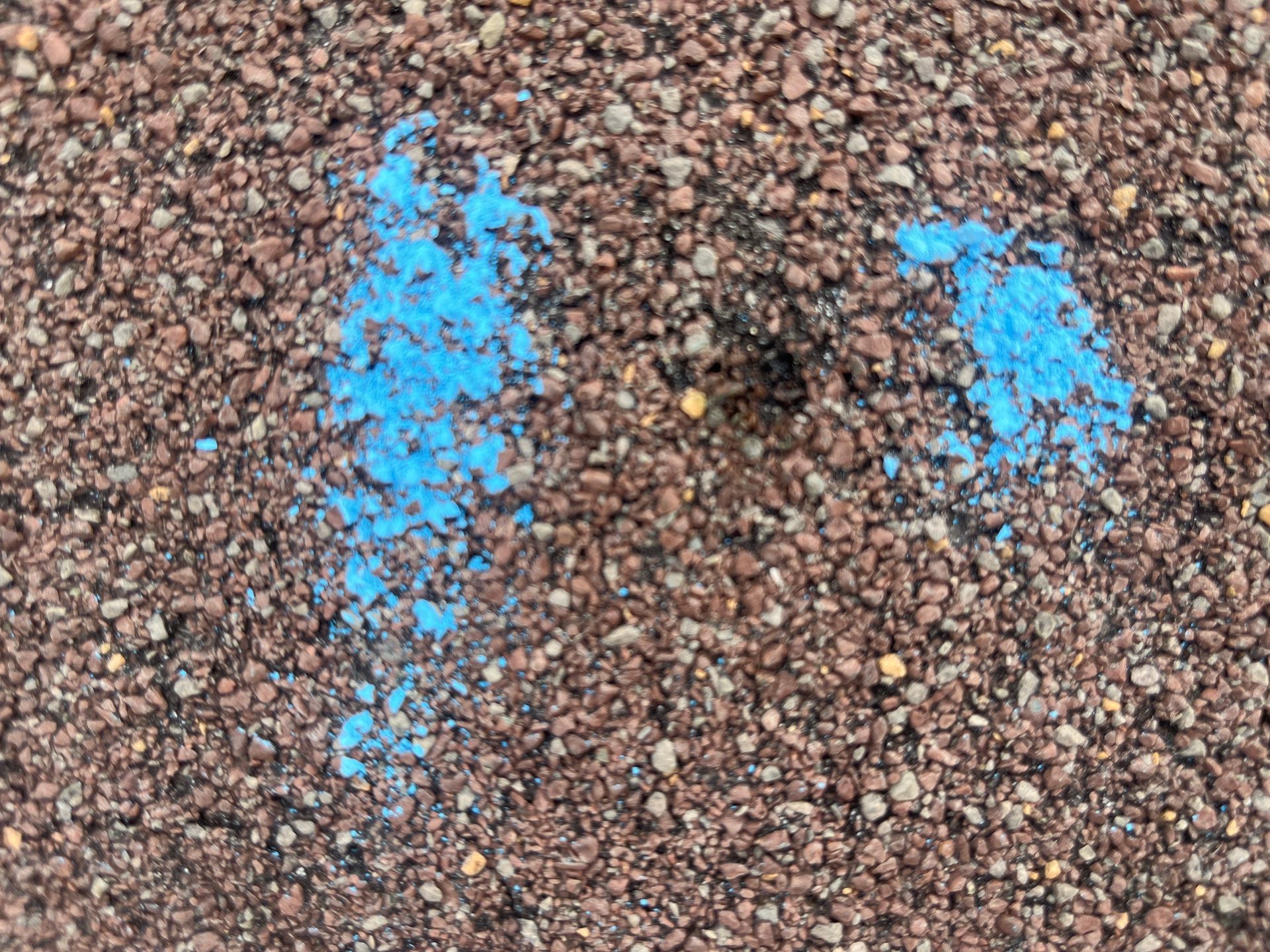 Blue paint splatters on a rough gravel surface, forming two irregular patches.