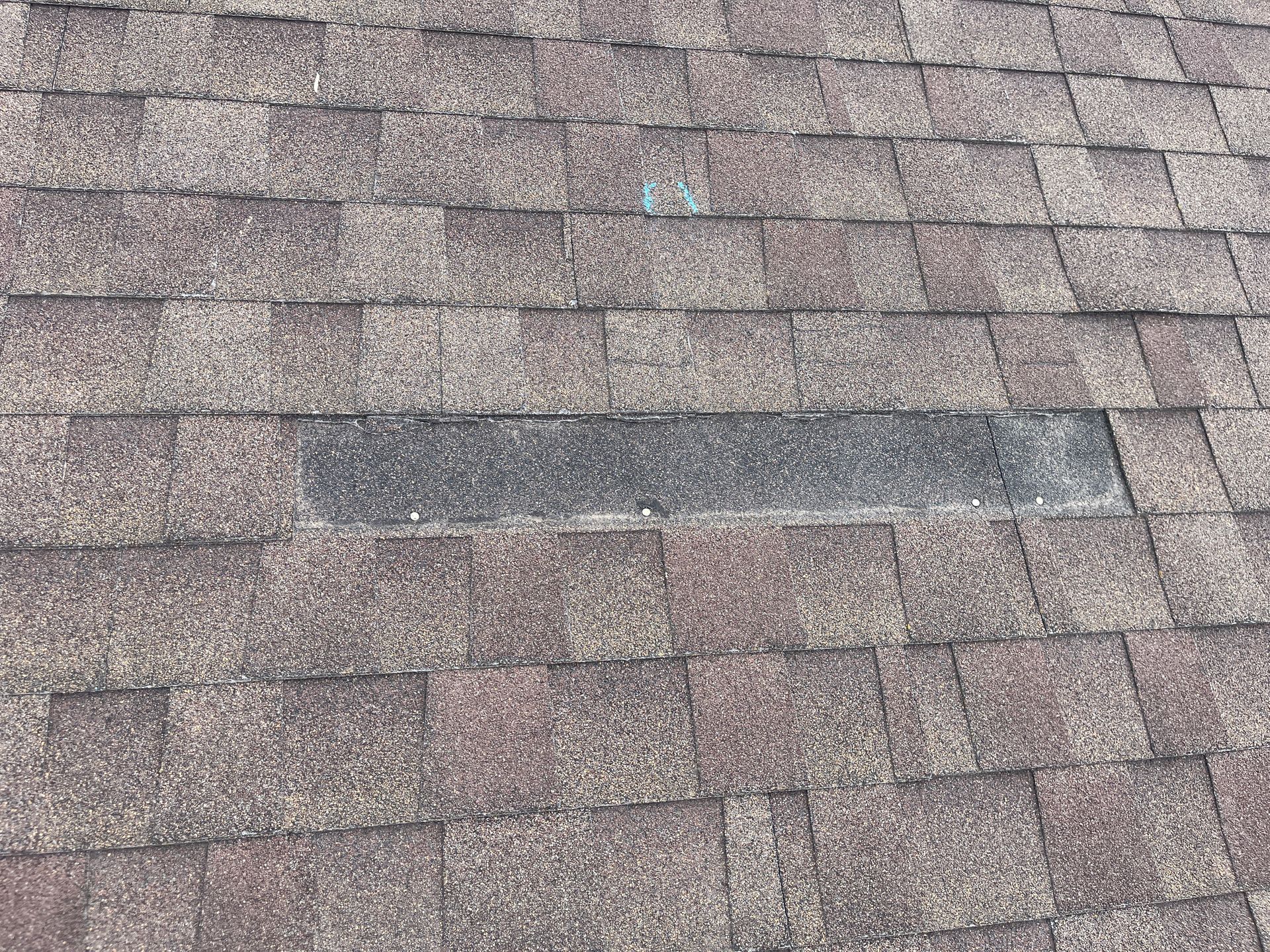 Close-up of weathered gray-brown roof shingles with a darker rectangular patch.