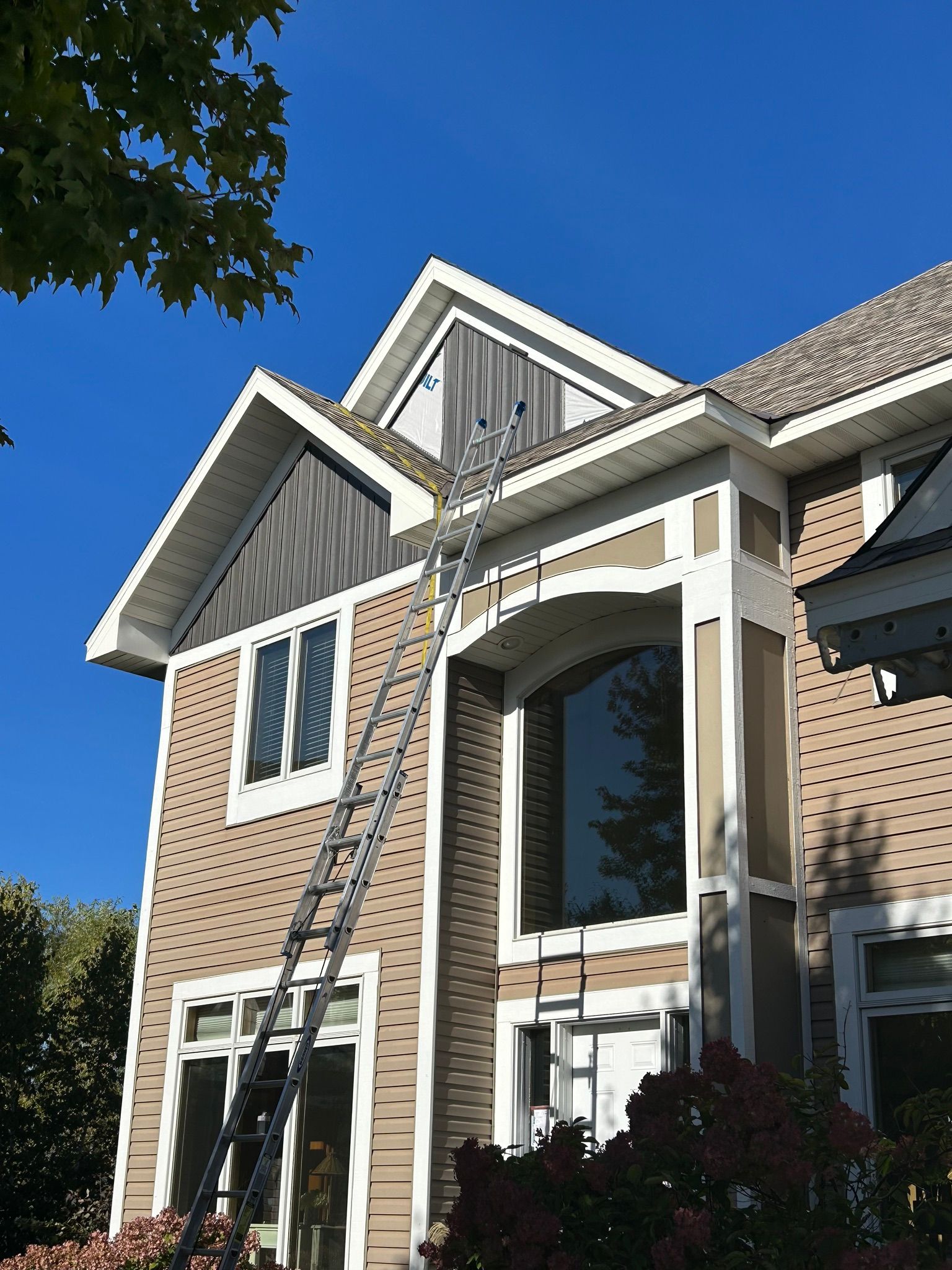 Brick house exterior with white trim, tall windows, and a peaked gable under a clear blue sky