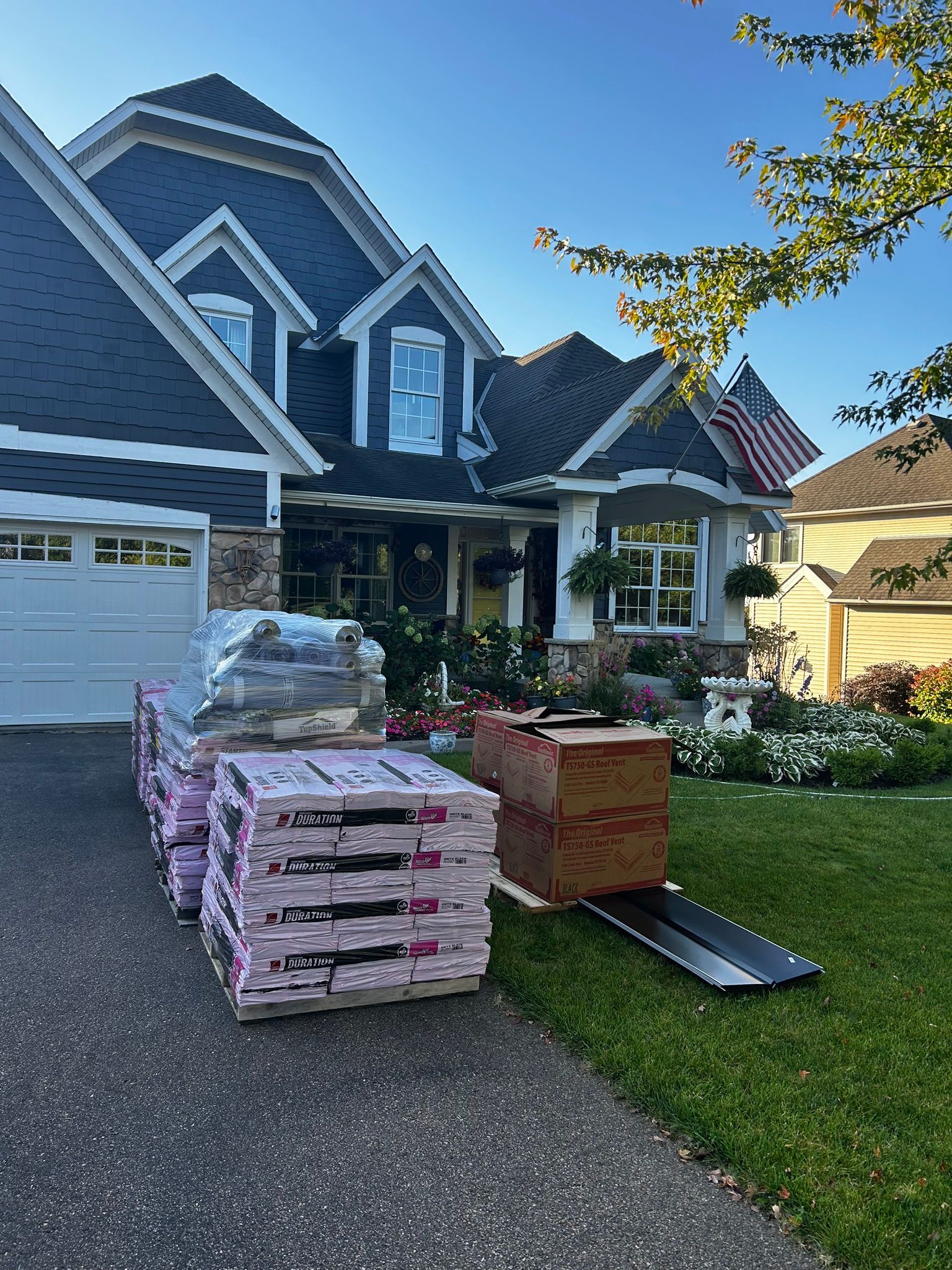 Pile of landscaping materials on a driveway outside a suburban house with a white garage and dark blue siding