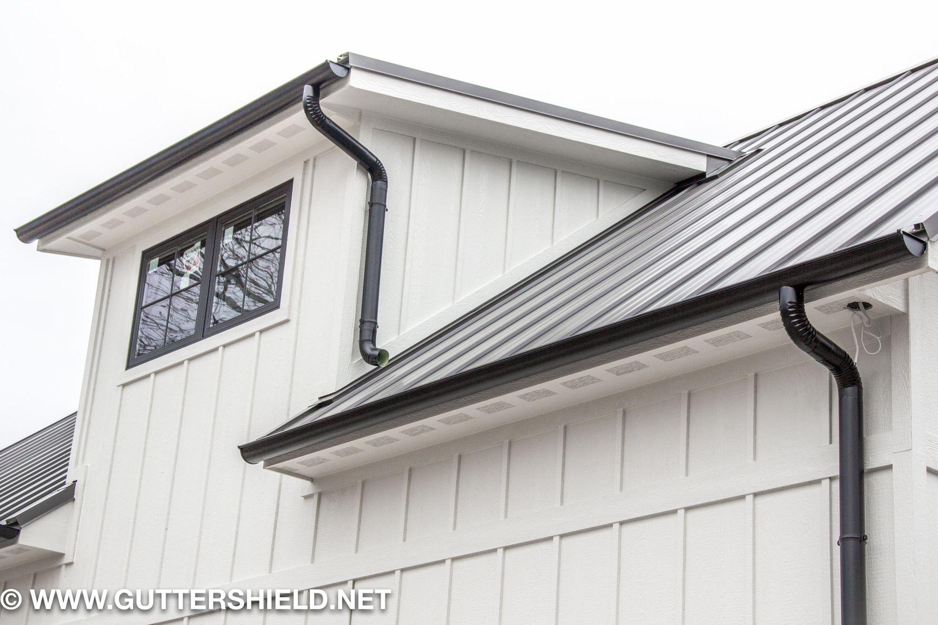 White house exterior with dark metal roof, black gutters, and a dormer window