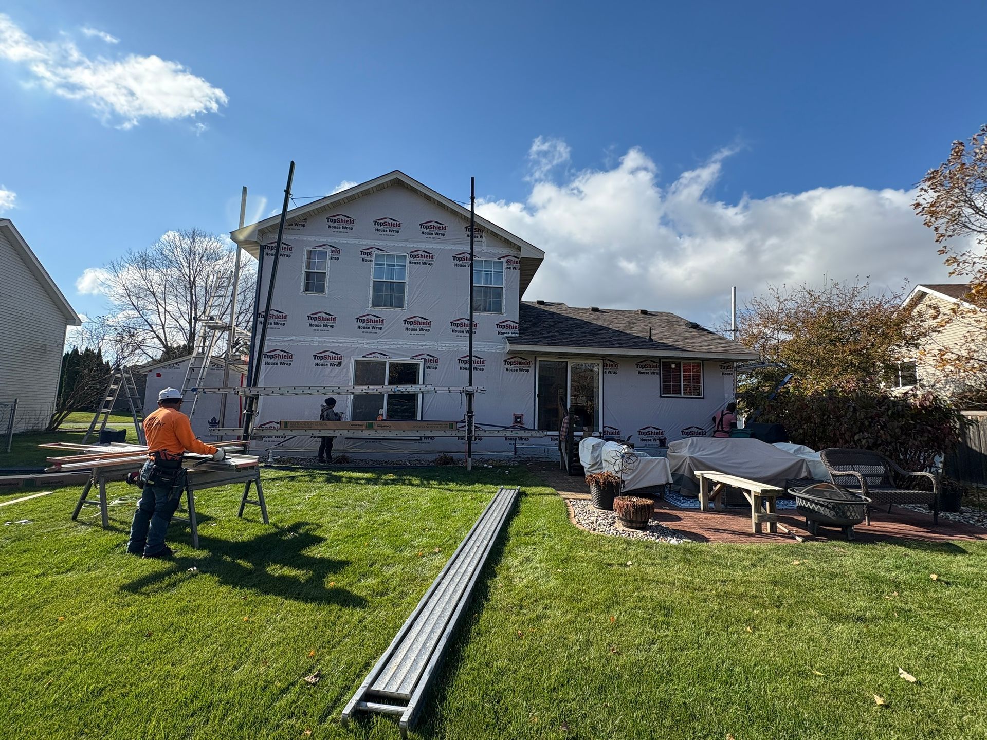 Workers laying materials in a grassy yard beside a white house under a blue sky.