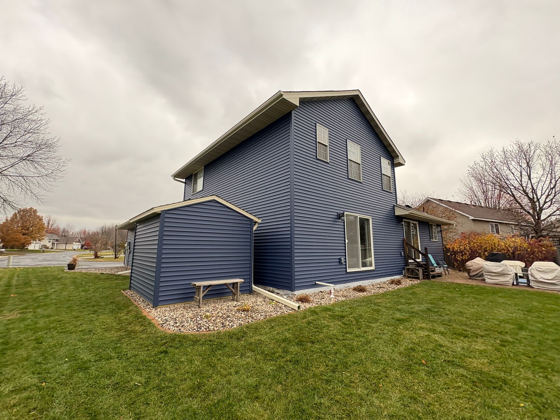 Blue corrugated house with curved walls and stone base on a grassy yard under overcast sky