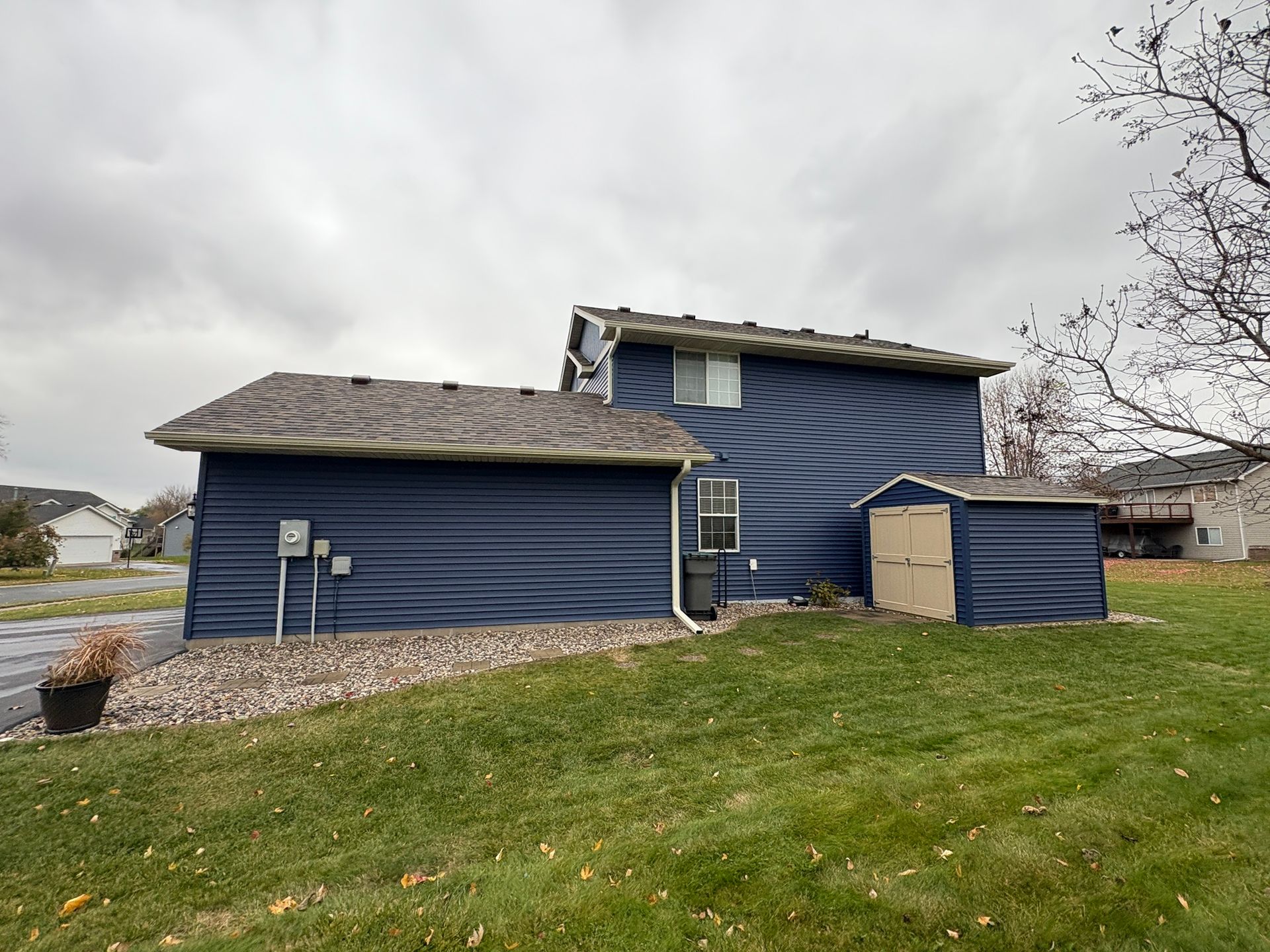 Blue house with damaged roof and siding beside a grassy slope under a cloudy sky