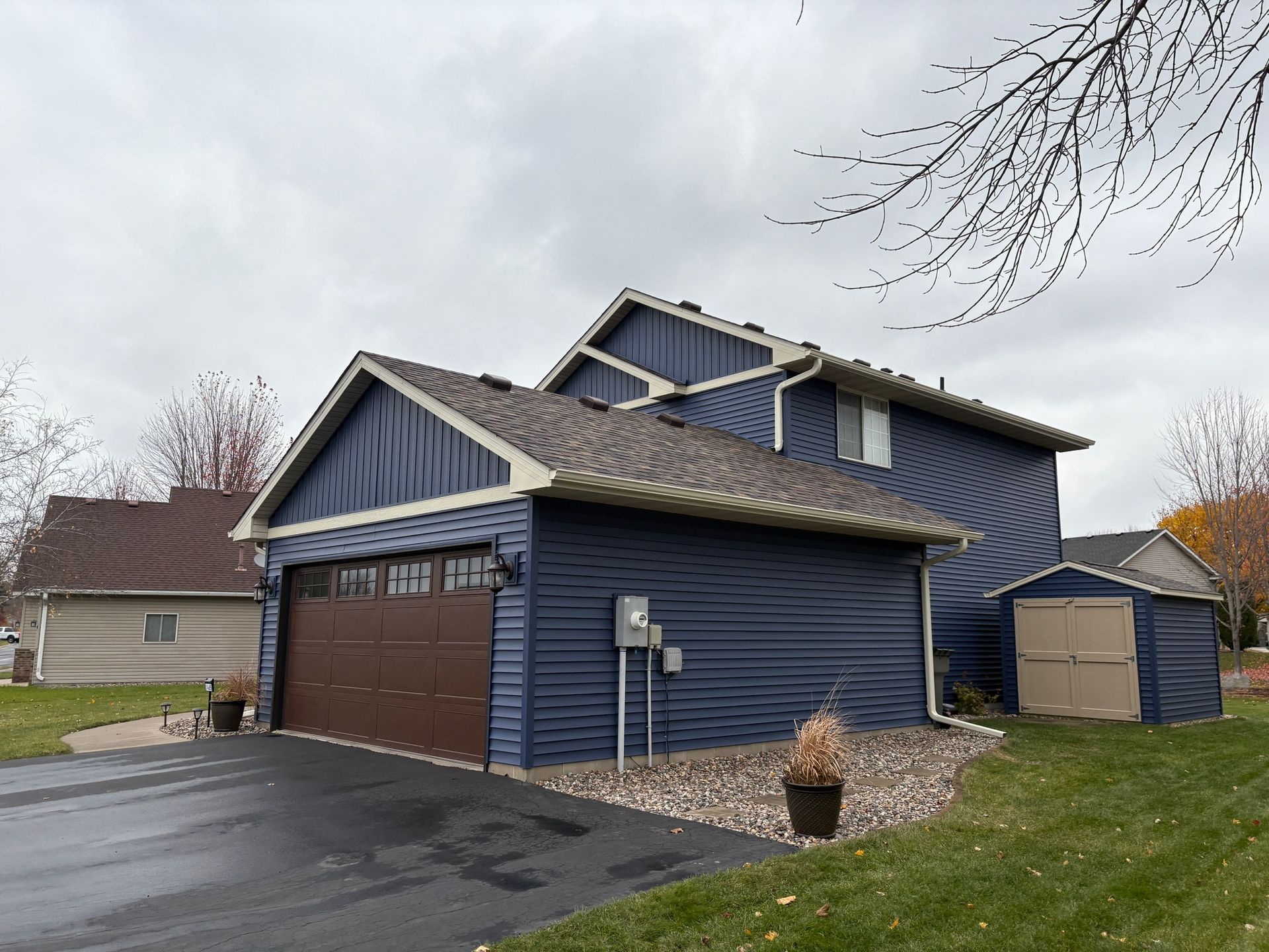 Blue house with brown garage door, stone landscaping, and driveway under a cloudy sky