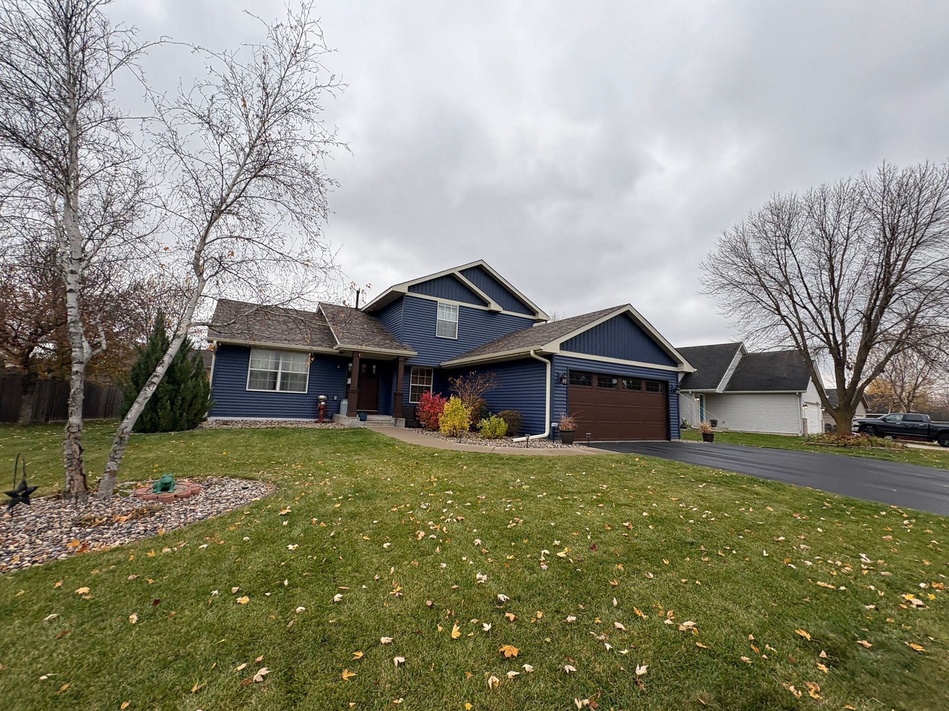 Blue house with a front porch and driveway on a cloudy day, with a grassy yard and bare trees