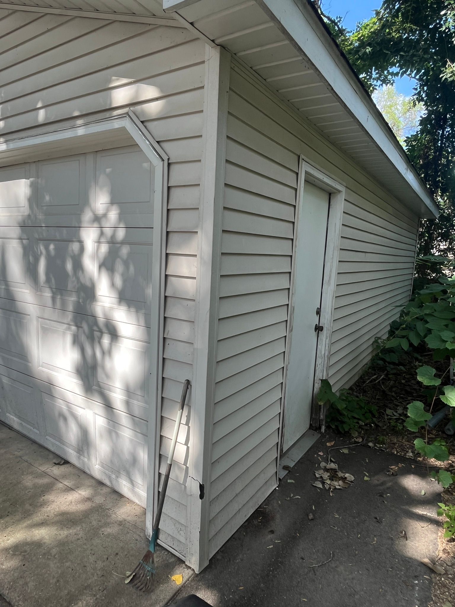 White garage and side door on a beige house exterior, with sunlight and tree shadows on the siding.