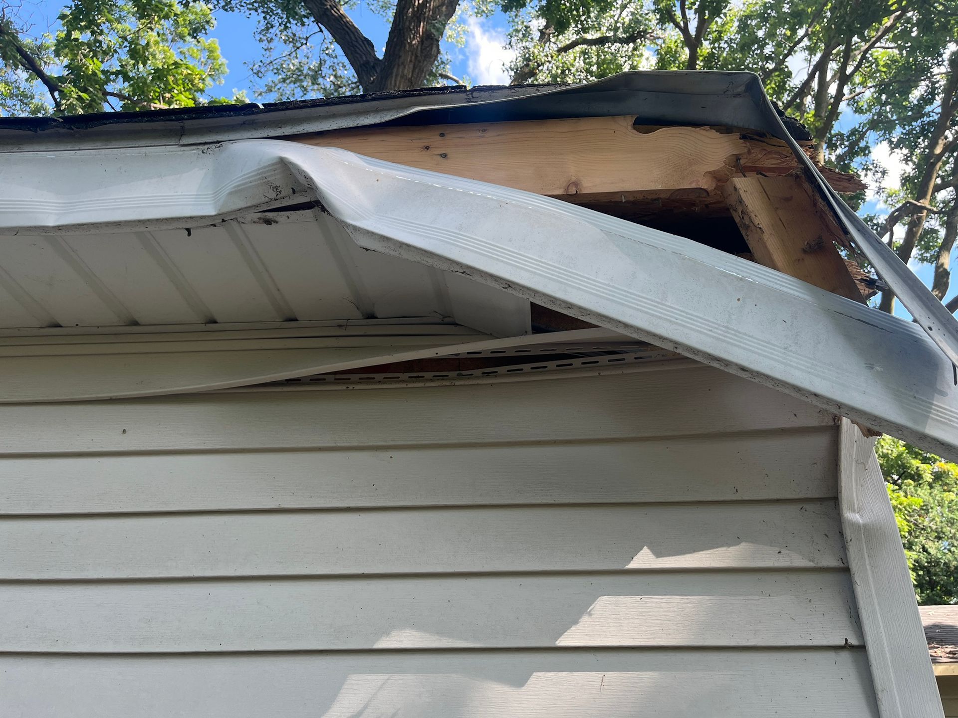 Damaged house roof with a bent white gutter and exposed wood under the eaves