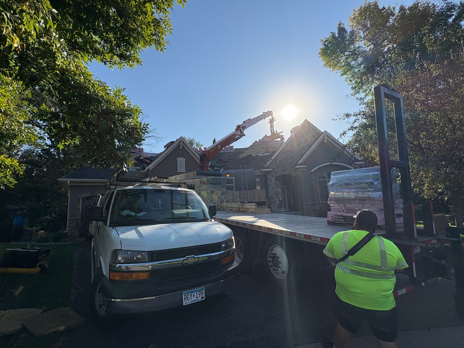 Tow truck loading a white van on a flatbed in front of a house, with a worker in a neon jacket nearby.