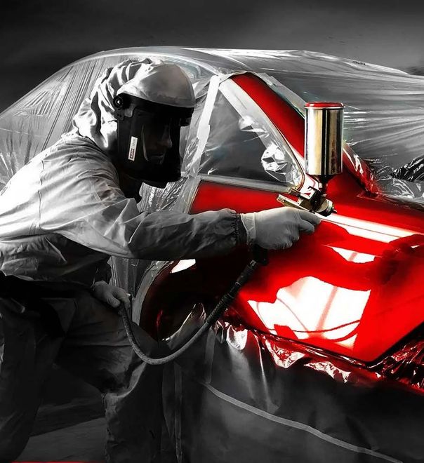 Spraying red paint on a car body in a workshop, with a protective suit and mask