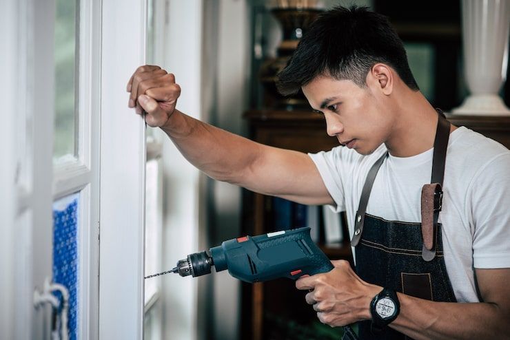 Worker drilling into a wall with a power drill while holding a stud or pipe in a construction setting