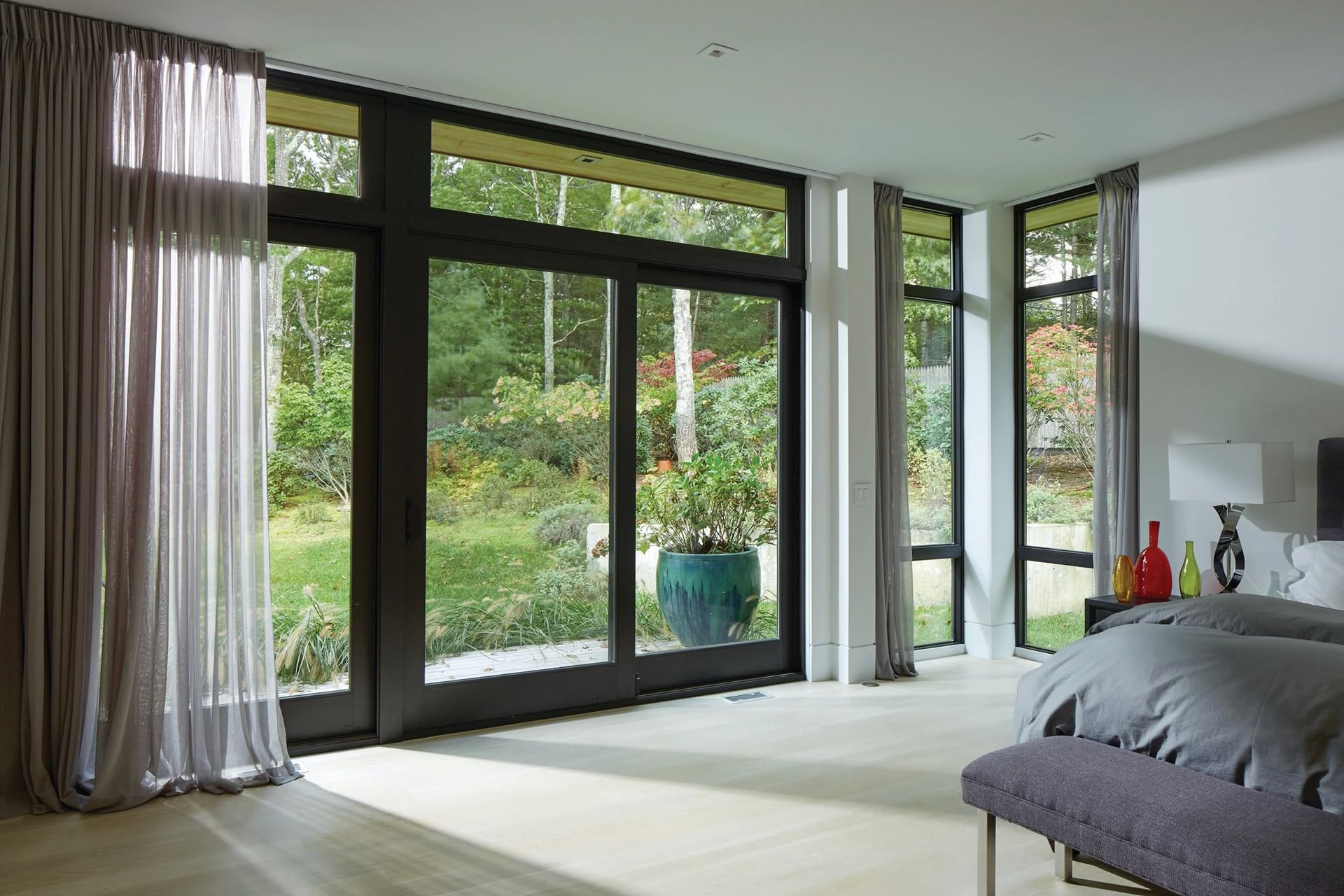 Modern bedroom with floor-to-ceiling glass doors, garden view, and a bed by the window.
