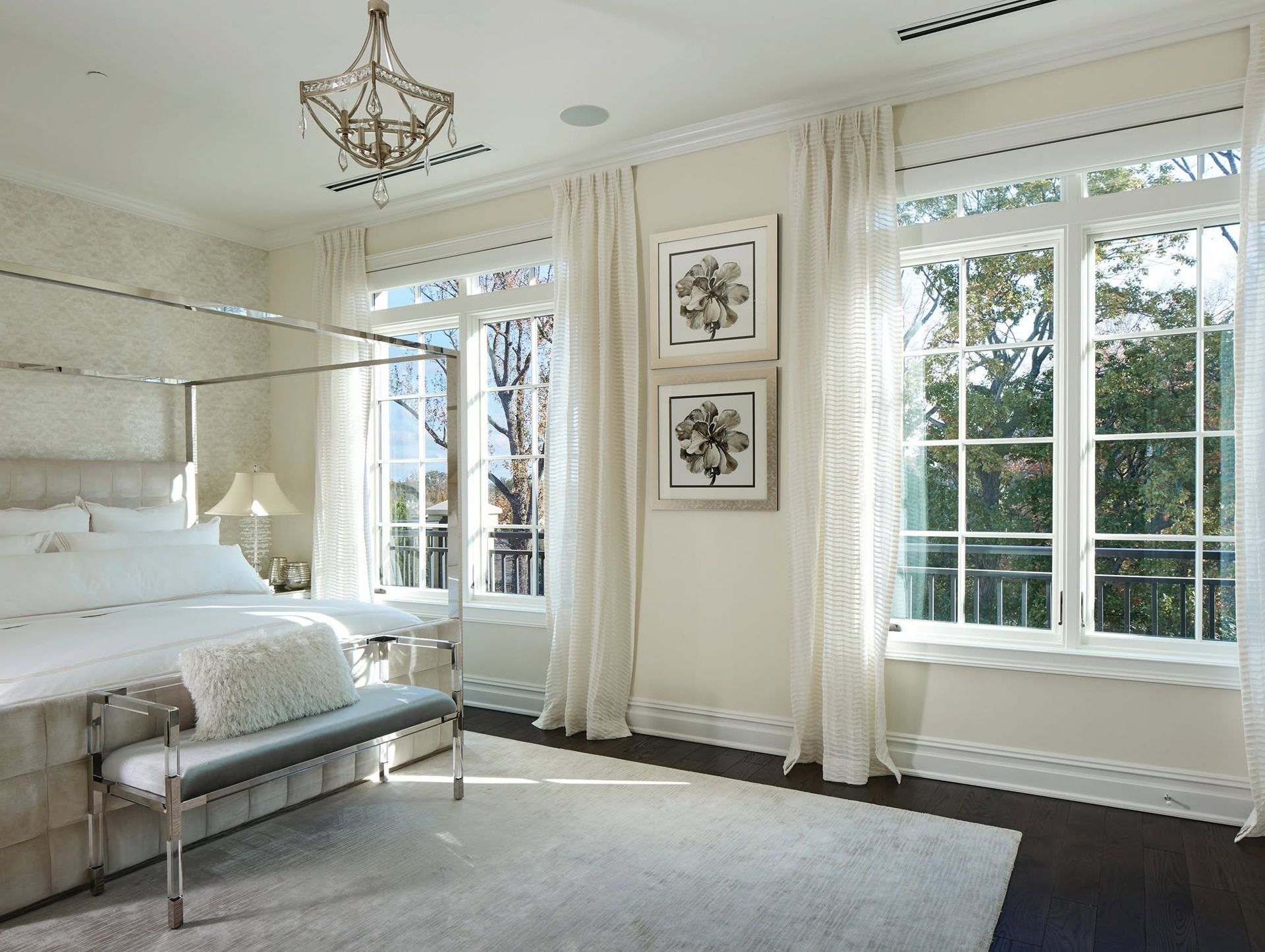 Bright bedroom with a canopy bed, white curtains, large windows, and a bench at the foot of the bed