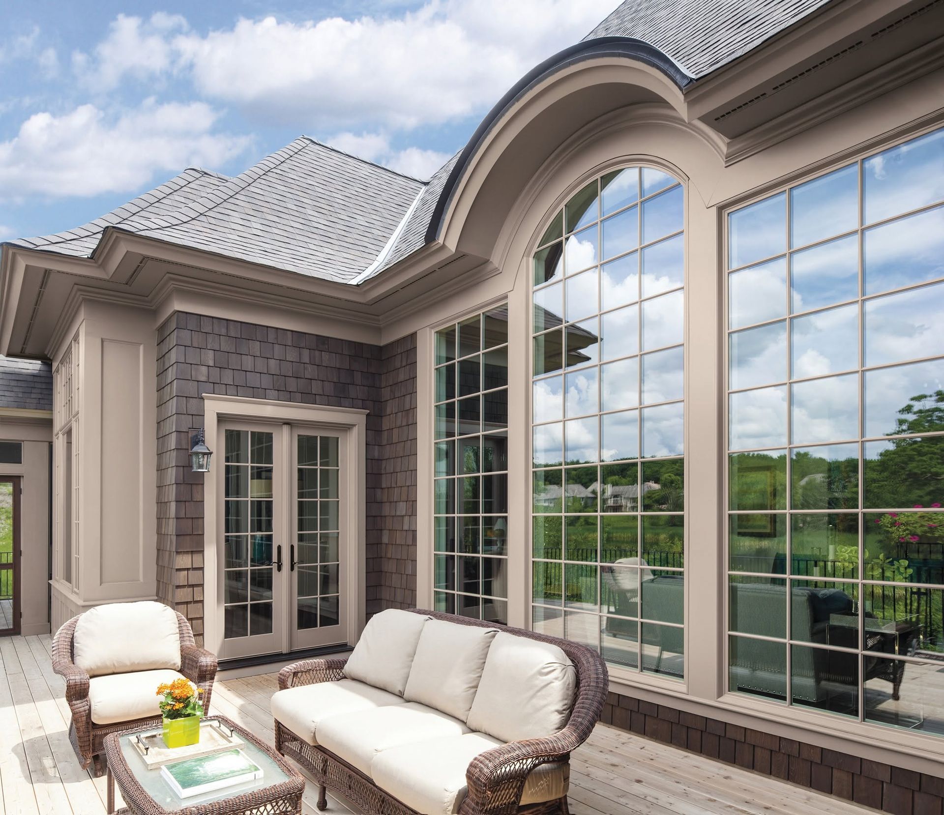 Elegant patio with white cushioned seating beside a large arched window and brick exterior.