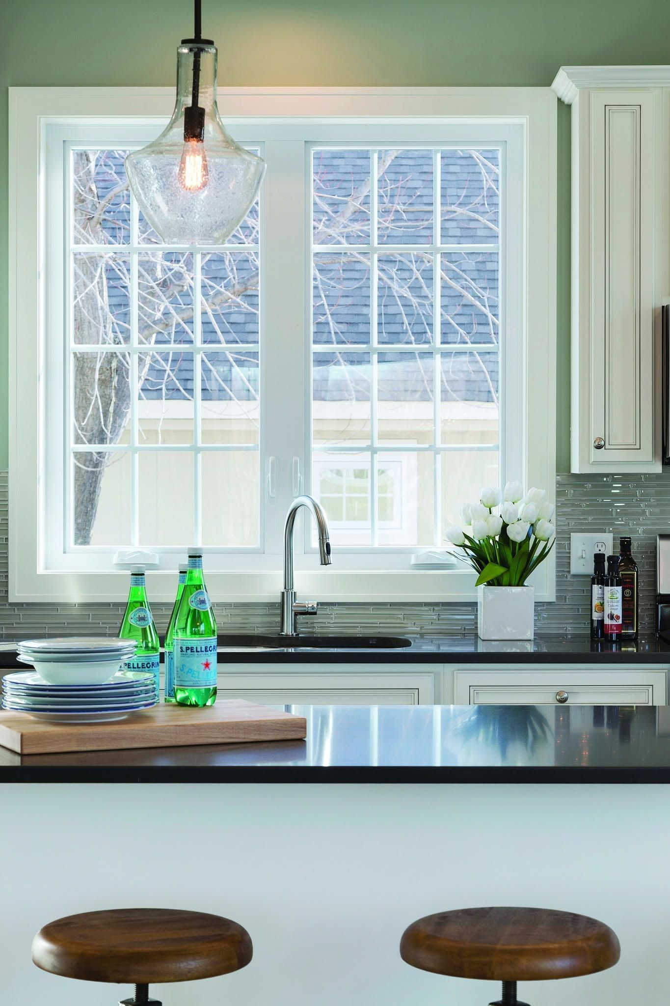 Bright kitchen with large window, sink, island, stools, and hanging light fixture.