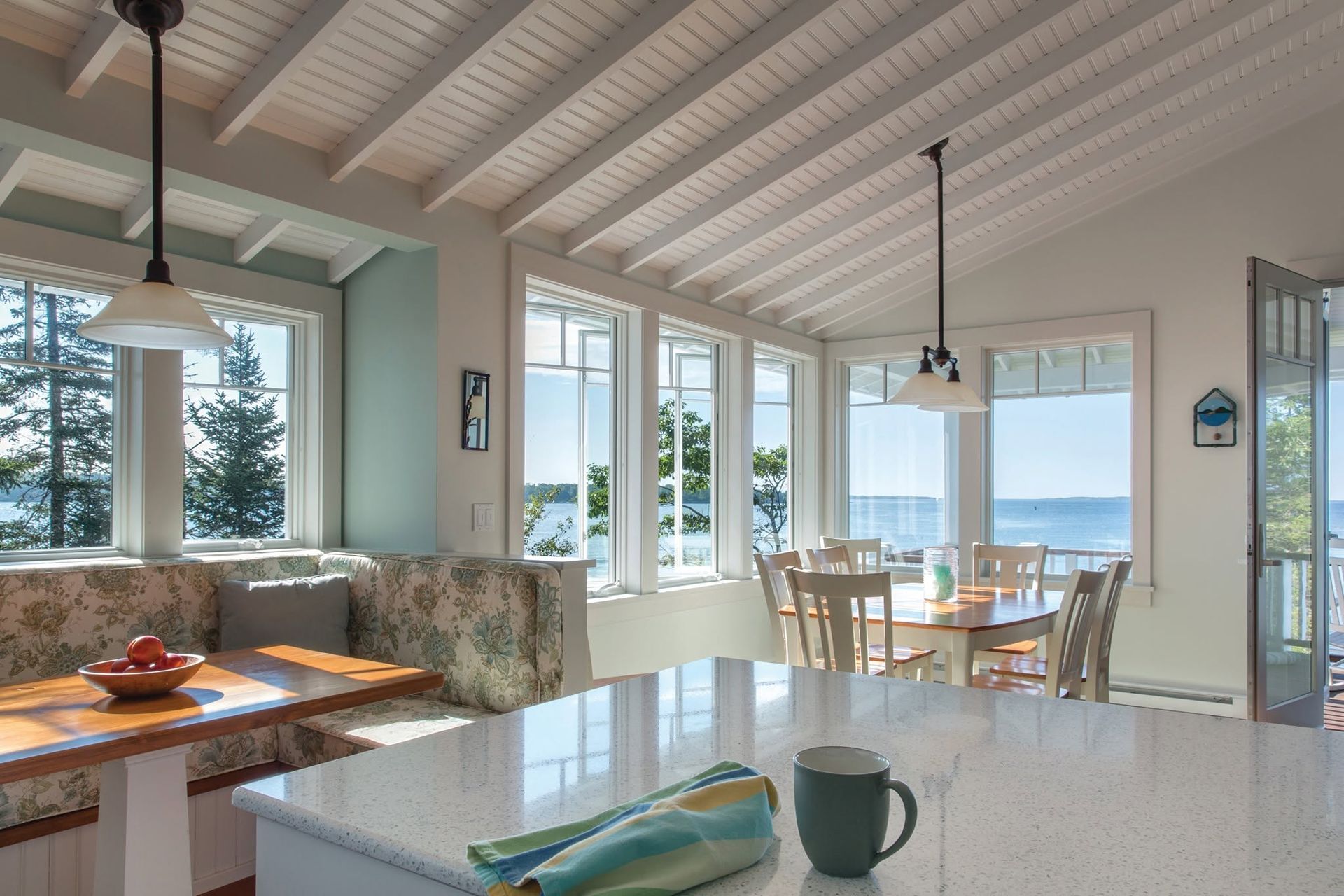 Bright living room with white beams, large windows, dining table, and ocean view