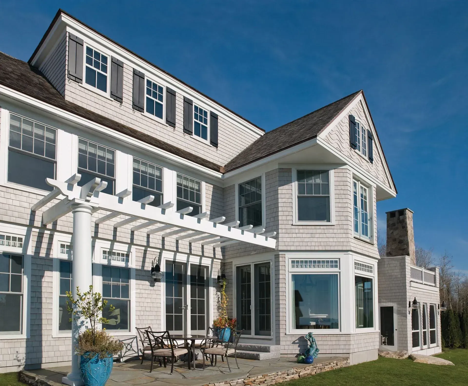 White seaside-style house with pergola patio, large windows, and blue sky.