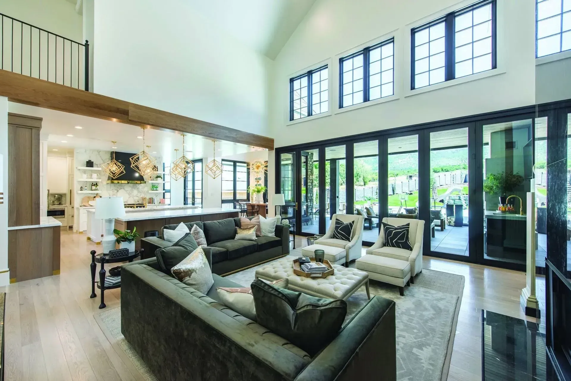 Modern open-plan living room with gray sectional, black chairs, and floor-to-ceiling glass doors overlooking greenery