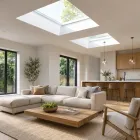 Bright modern living room with skylights, beige sectional sofa, wooden coffee table, and open kitchen.