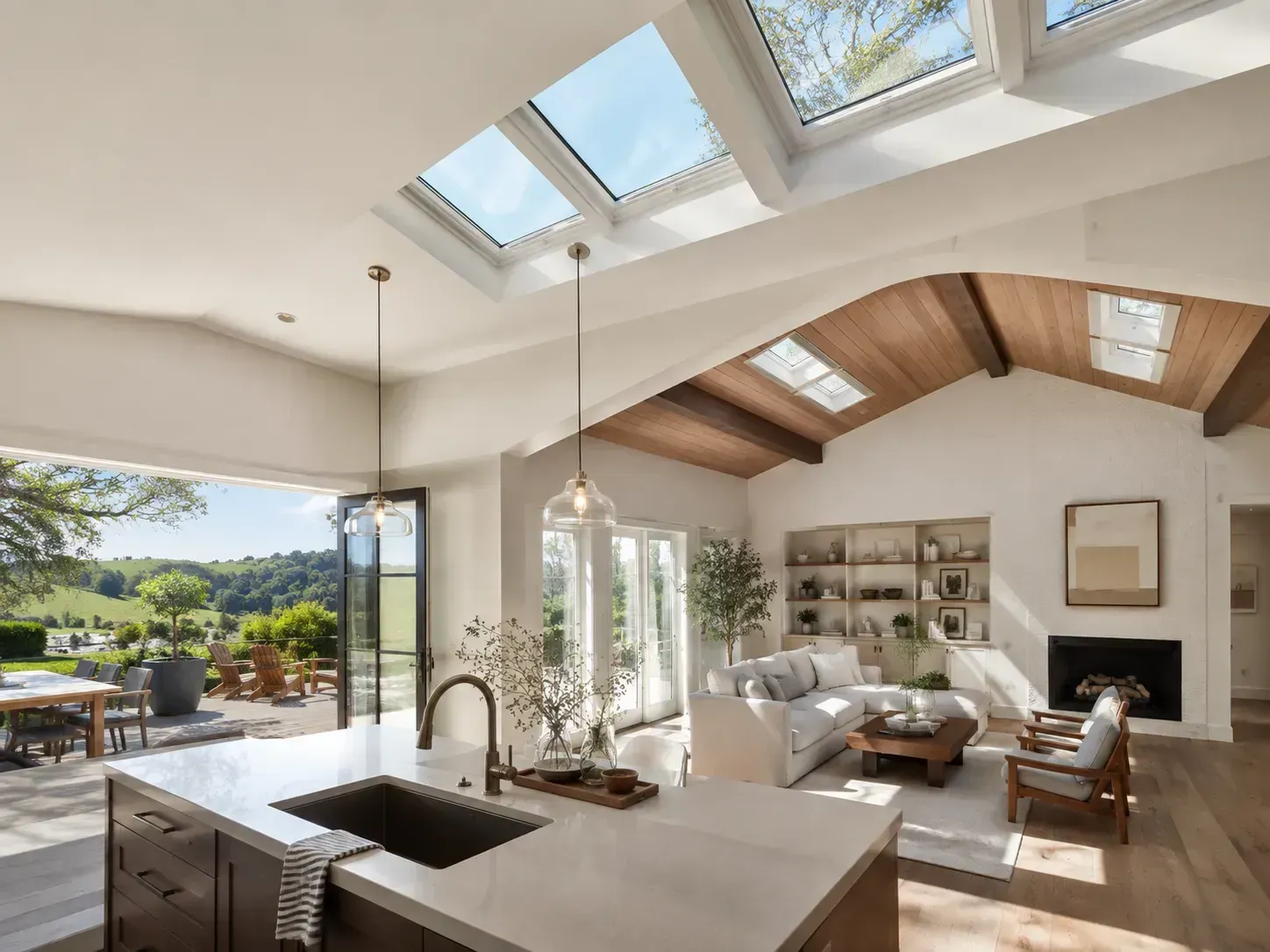 Open-plan living room with skylights, fireplace, and kitchen island opening to a sunny patio and garden