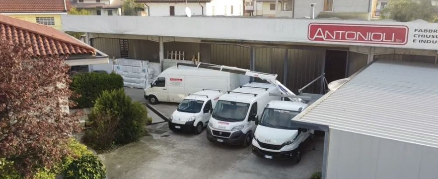 Parcheggio con tre furgoni bianchi e un camion bianco accanto a un edificio con l'insegna Antonini.