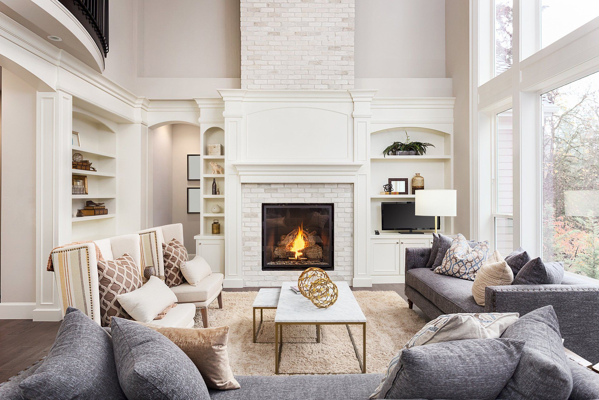 Bright living room with white fireplace, gray sofas, and large windows.