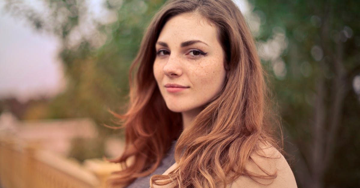 Woman looking at the camera, with a neutral expression. Outside with a blurred background.