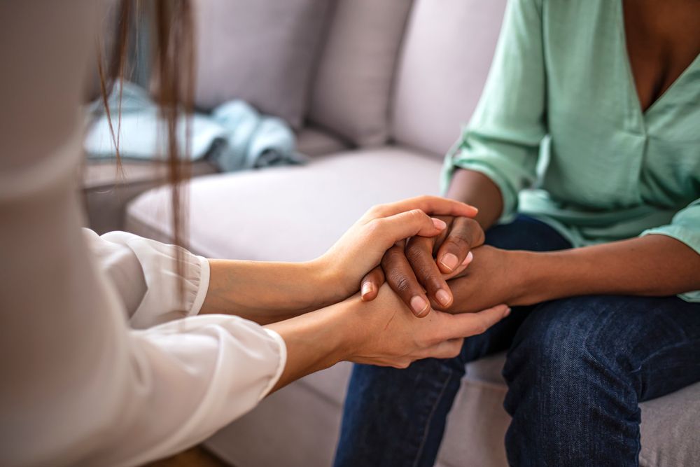 A woman is holding another woman 's hand while sitting on a couch.