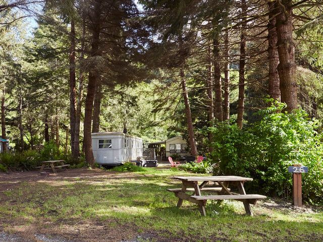 Wooded campsite with a white trailer, picnic table, and green trees in shade