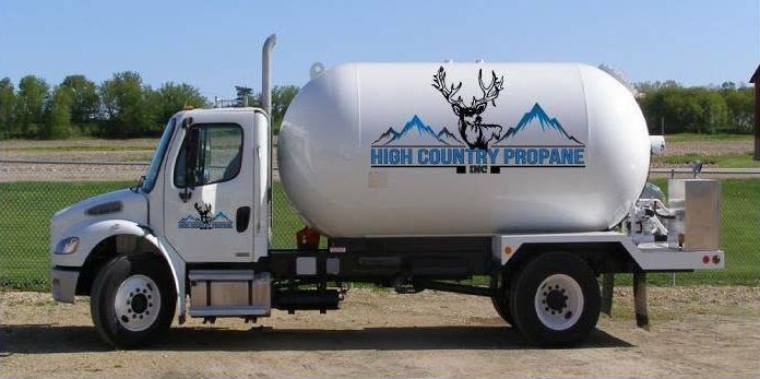 White propane delivery truck with deer logo parked on a dirt lot under a blue sky