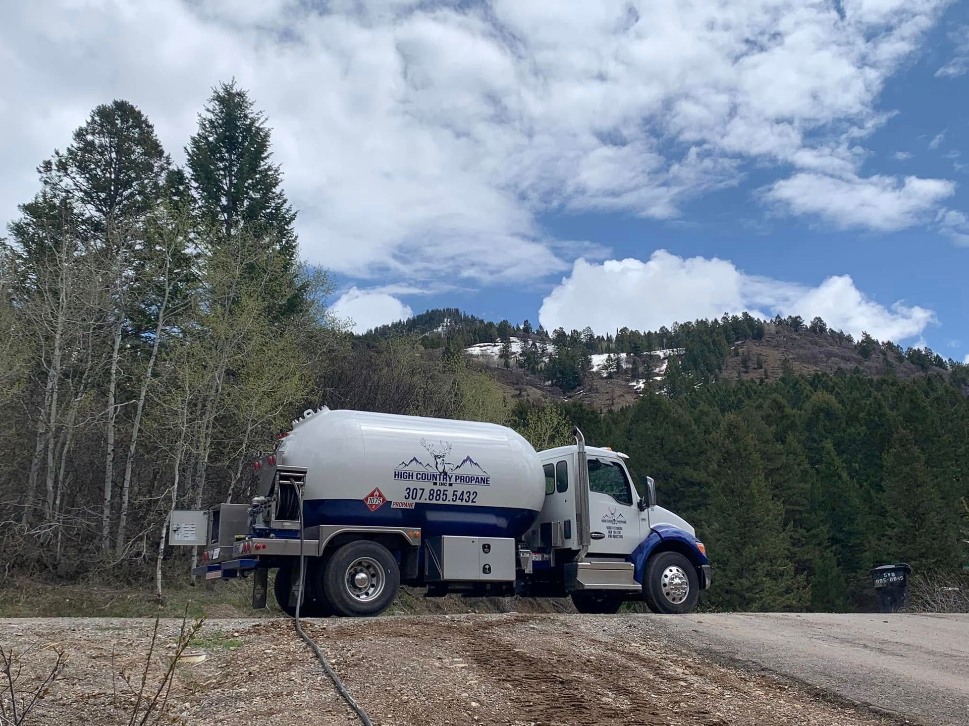 White water truck parked on a dirt road beside trees and mountains under a cloudy sky