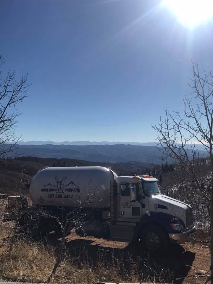 White tanker truck on a hillside with mountains in the distance under a bright blue sky.