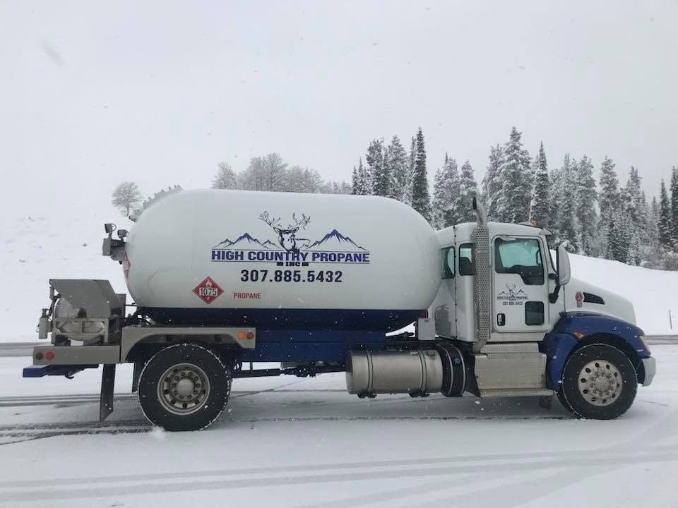 Blue-and-white tanker truck parked in a snowy forest with logo and phone number on the tank