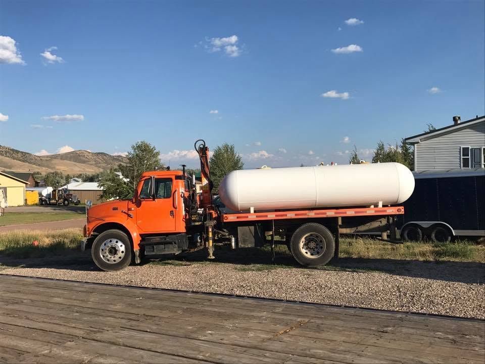 Orange tanker truck parked on gravel beside a railroad crossing under a clear blue sky