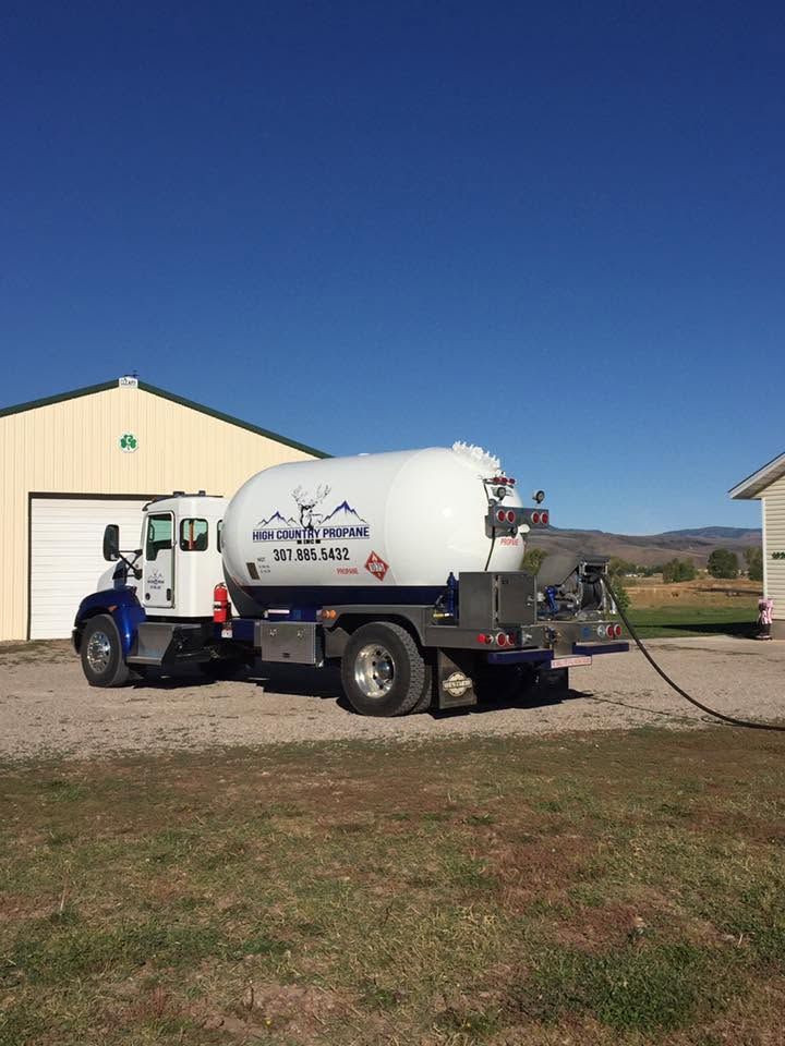 White utility truck with tank parked beside a beige building on a rural lot under a clear blue sky