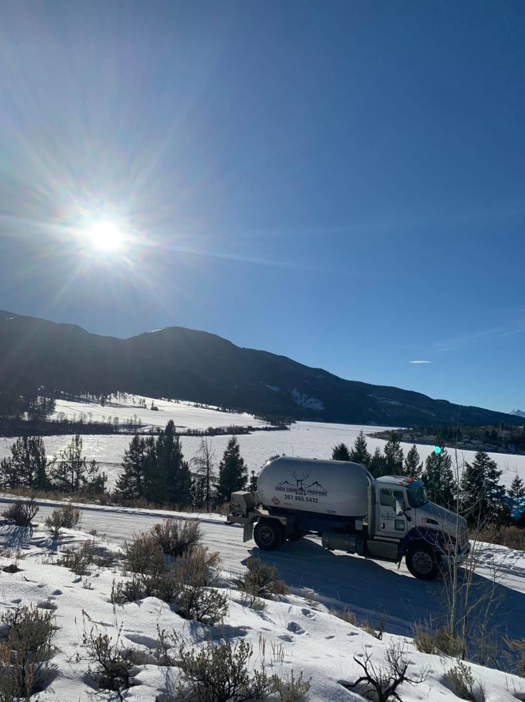 Snowy mountain landscape with a white truck driving through a sunlit winter field.