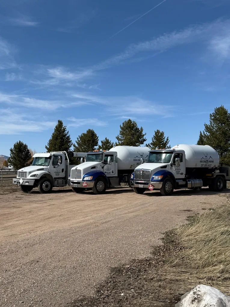Three tanker trucks parked on a gravel lot under a clear blue sky