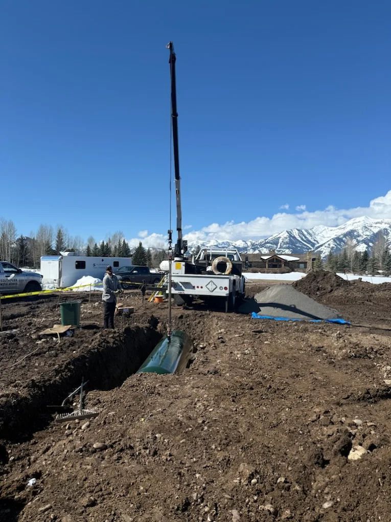 Construction drilling rig on a dirt site with mountains in the background under a clear blue sky