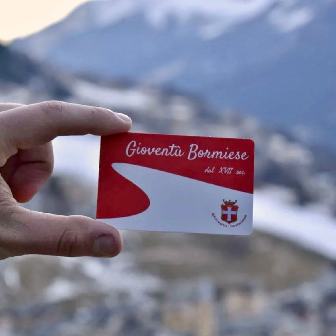Una persona ha in mano un cartellino bianco e rosso con la scritta giovanta bormise