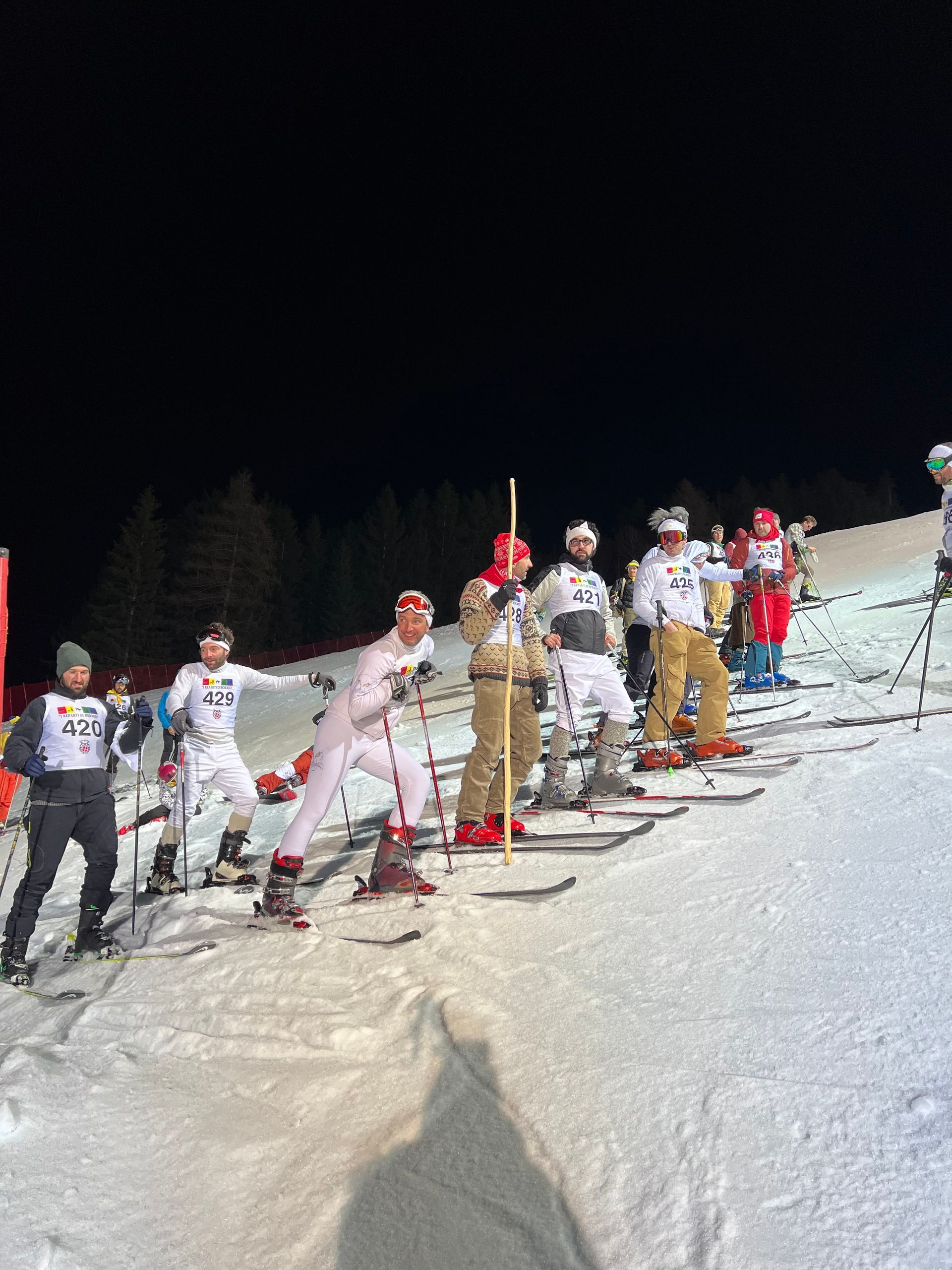 Un gruppo di persone sta sciando lungo un pendio innevato di notte.
