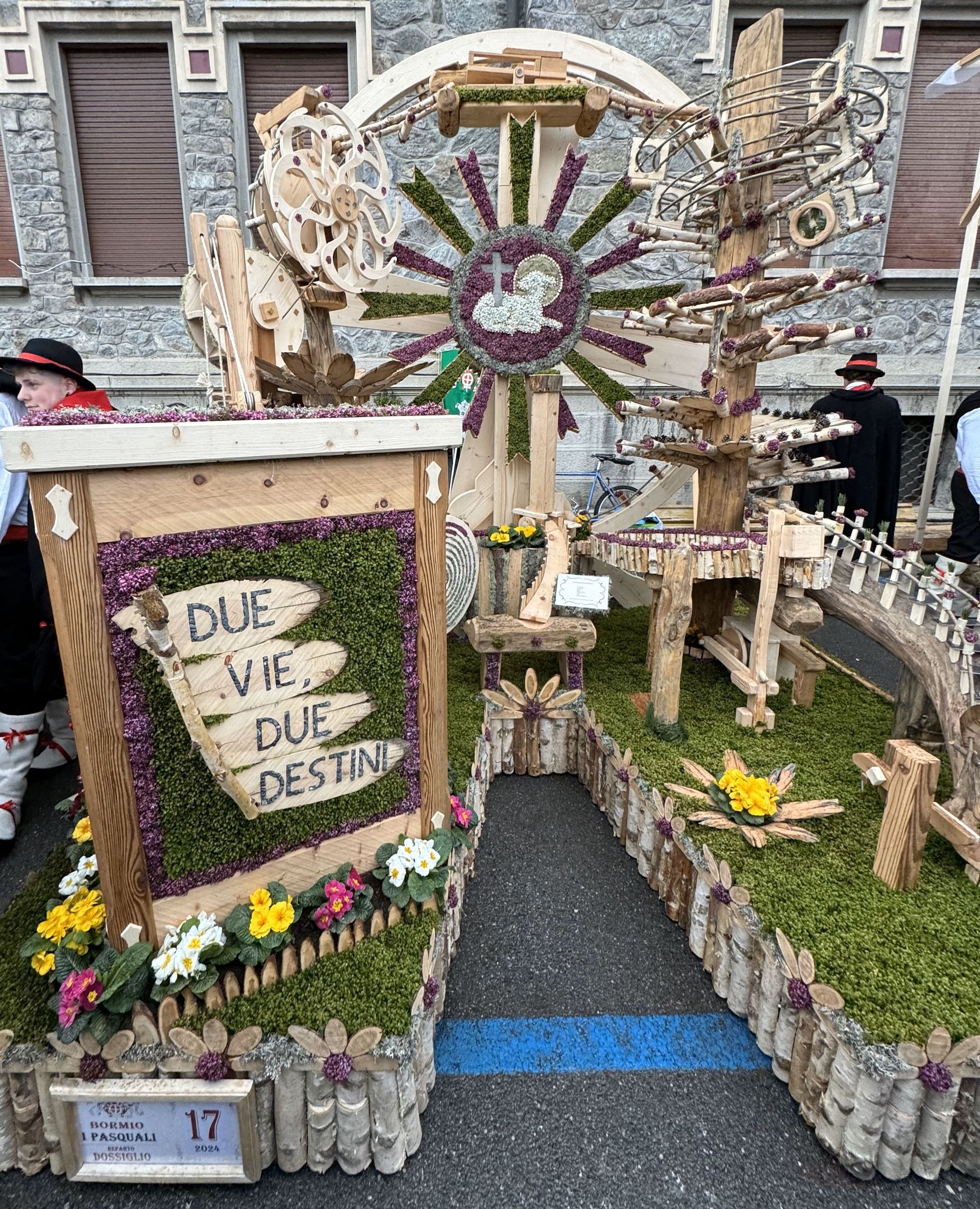 Una ruota panoramica fatta di legno e fiori è esposta in una parata.