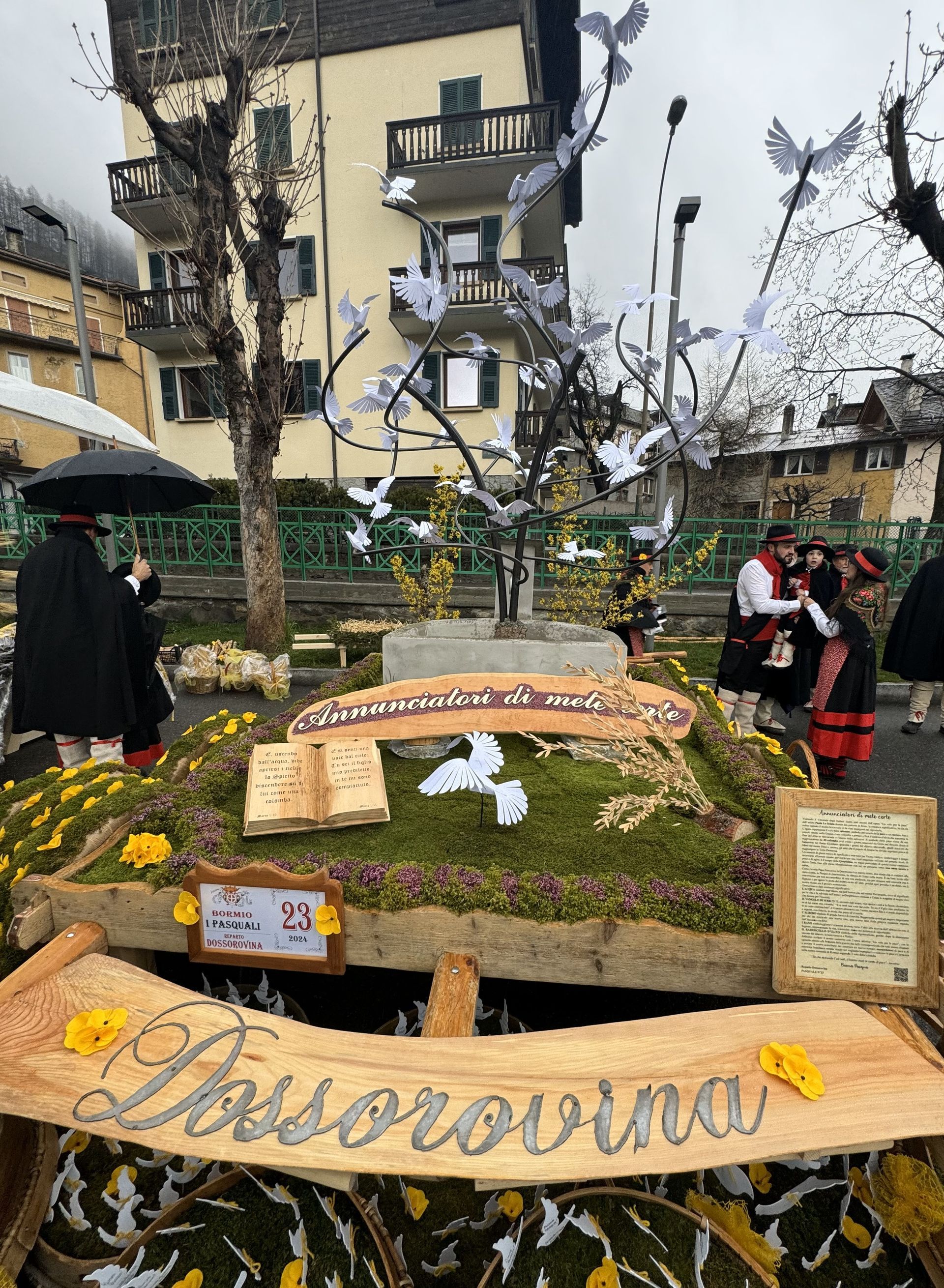 Un gruppo di persone sta in piedi attorno ad un'esposizione di fiori e ad un cartello con la scritta 