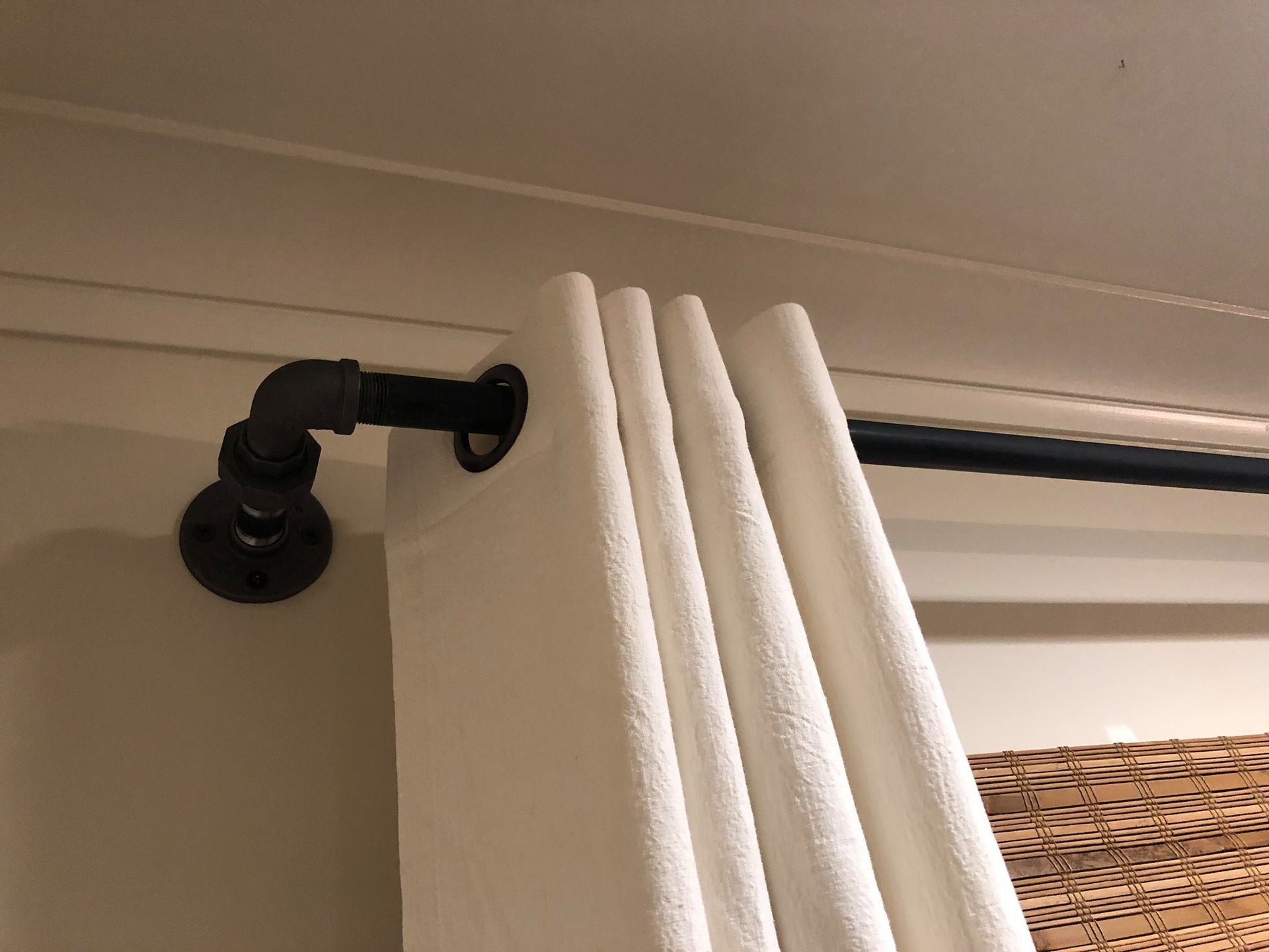 A pair of white curtains are hanging on a black pipe.