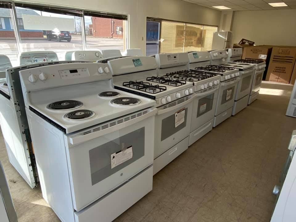 Row of white gas and electric stoves displayed in a showroom with large windows